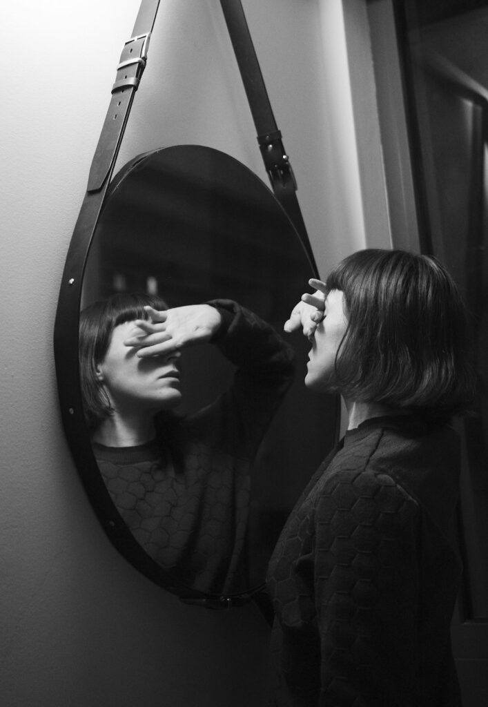 Mujer frente al espejo tapándose los ojos, atrapada en las frases que se repite tras una ruptura