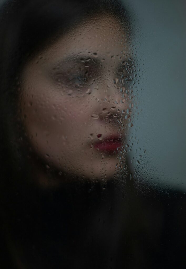 Rostro de mujer detrás de un cristal mojado por la lluvia